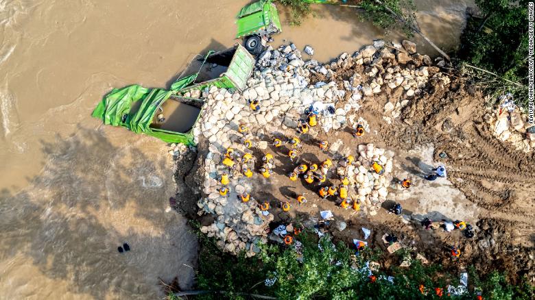 People dump trucks into floodwaters in an effort to mend the breach on a levee of Weihe River in Xunxian county in central China's Henan province Friday, July 23