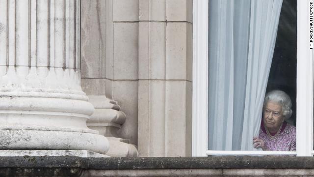 The monarch peers through the curtains of Buckingham Palace as she waits for The Patrons Lunch to start on the Mall in central London on June 12, 2016. 