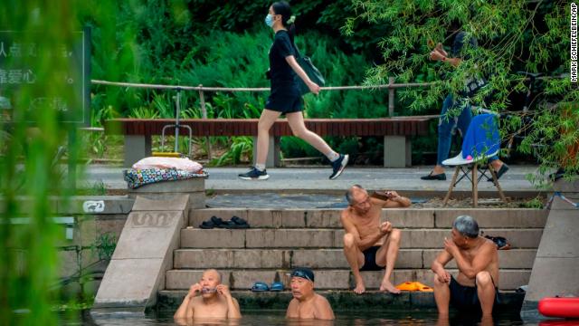 A woman walks past as men swim in a waterway in Beijing on August 2/