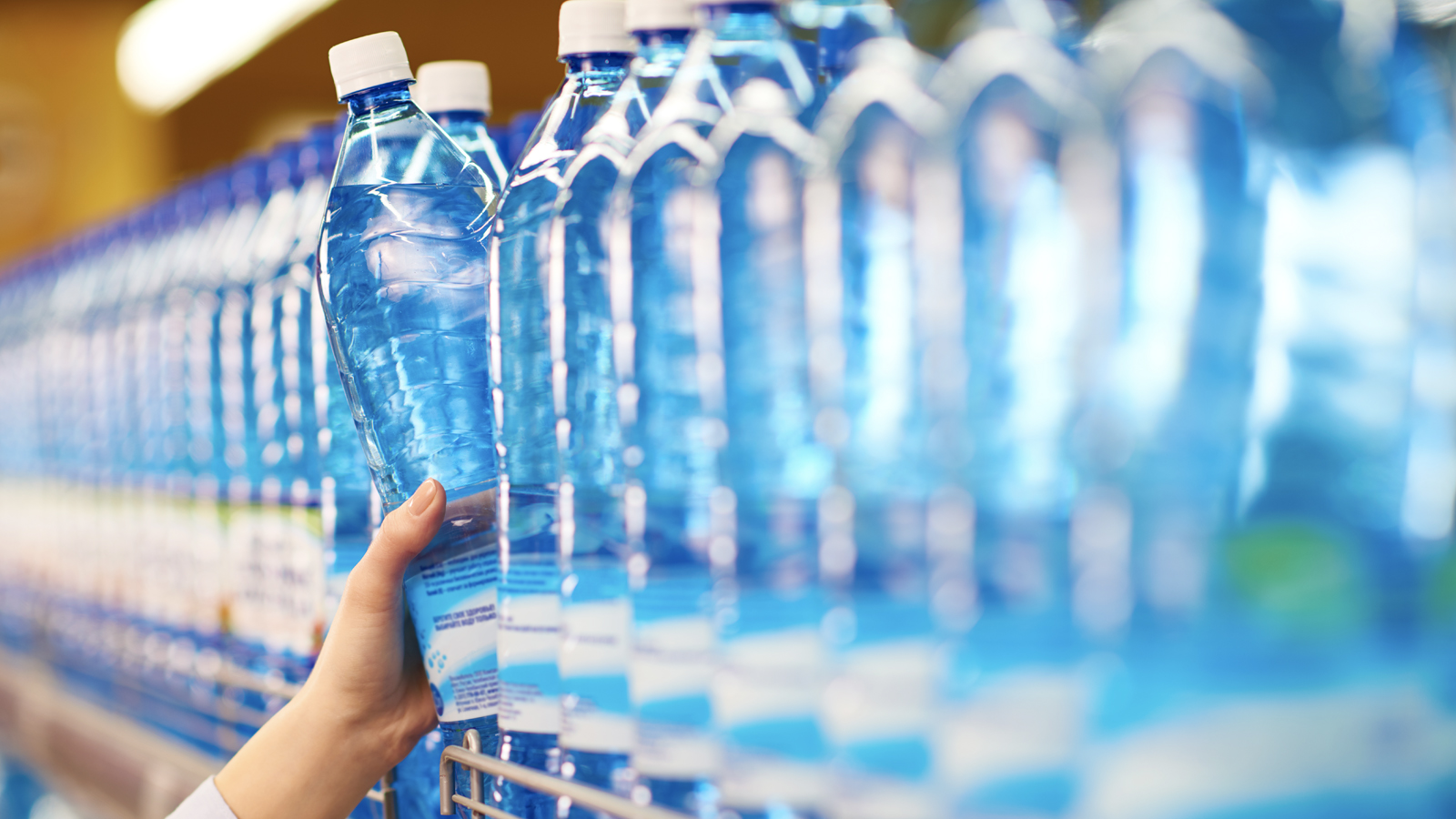 Hand taking bottled mineral water from shelf in food store