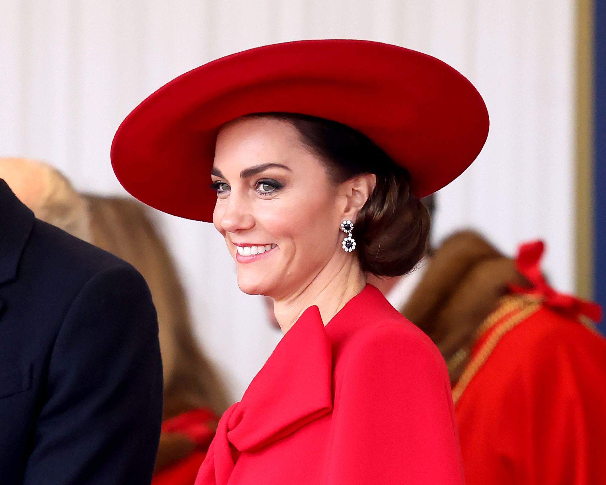 Catherine, Princess of Wales smiling in a bright red hat attending a ceremonial welcome for The President and the First Lady of the Republic of Korea at Horse Guards Parade on November 21, 2023 in London, England.