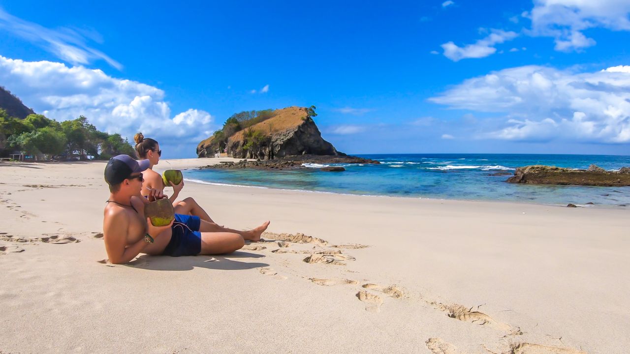 Two people lounging on a beach drinking from coconuts.