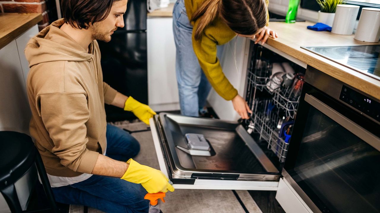 Two people cleaning a dishwasher