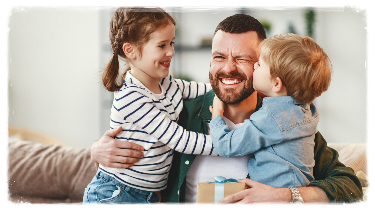 Dad hugging his kids with a gift in his hand.