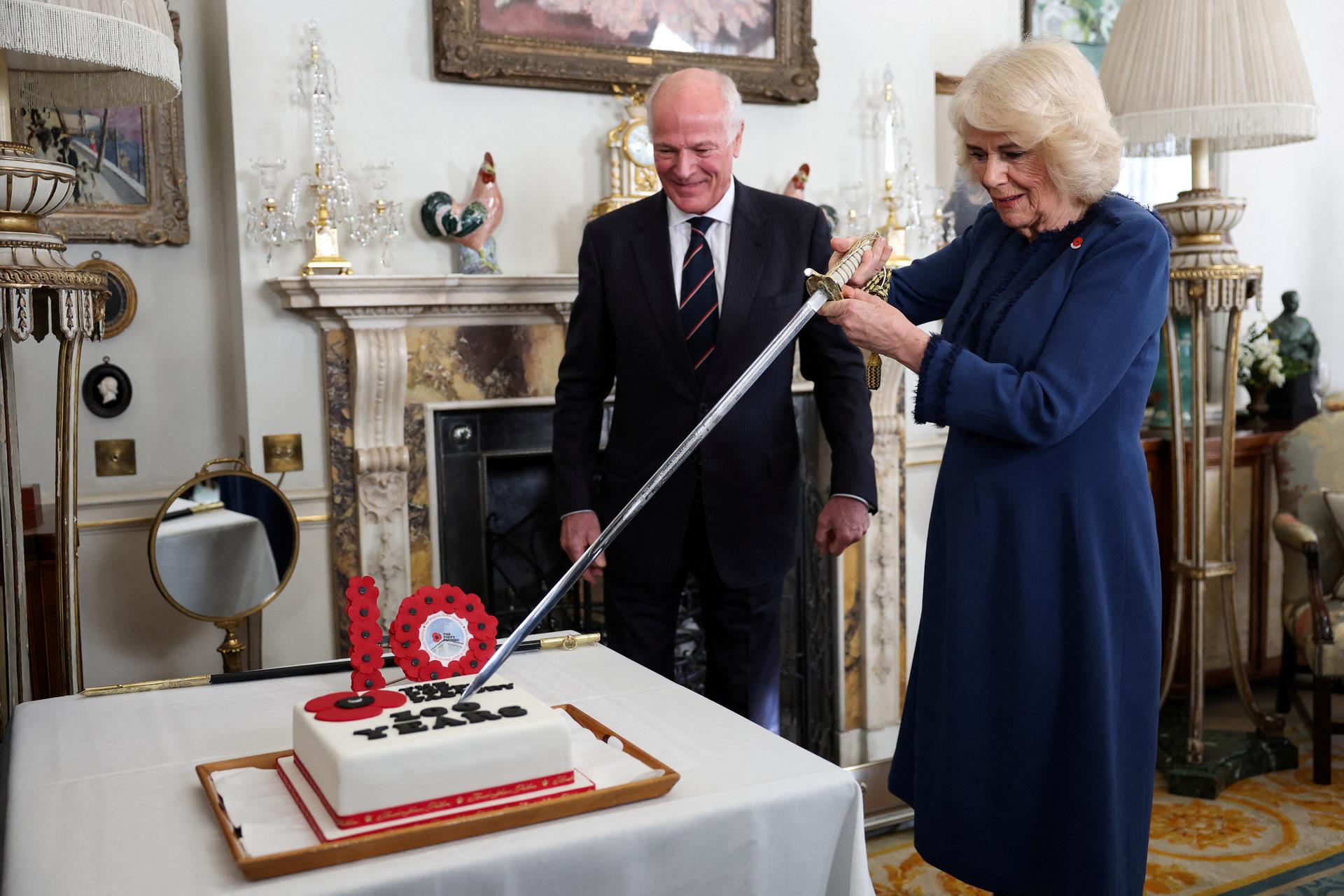 Britain's Queen Camilla (R) cuts a cake next to President of The Poppy Factory Surgeon Rear Admiral Lionel Jarvis (L) during a reception at Clarence House, in London, on February 15, 2024.