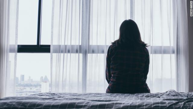 A woman sits on the side of a bed on an overcast day