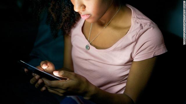 A young person looks at a smartphone in the dark