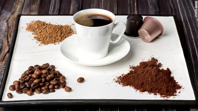 A cup of coffee is surrounded by coffee grounds and beans