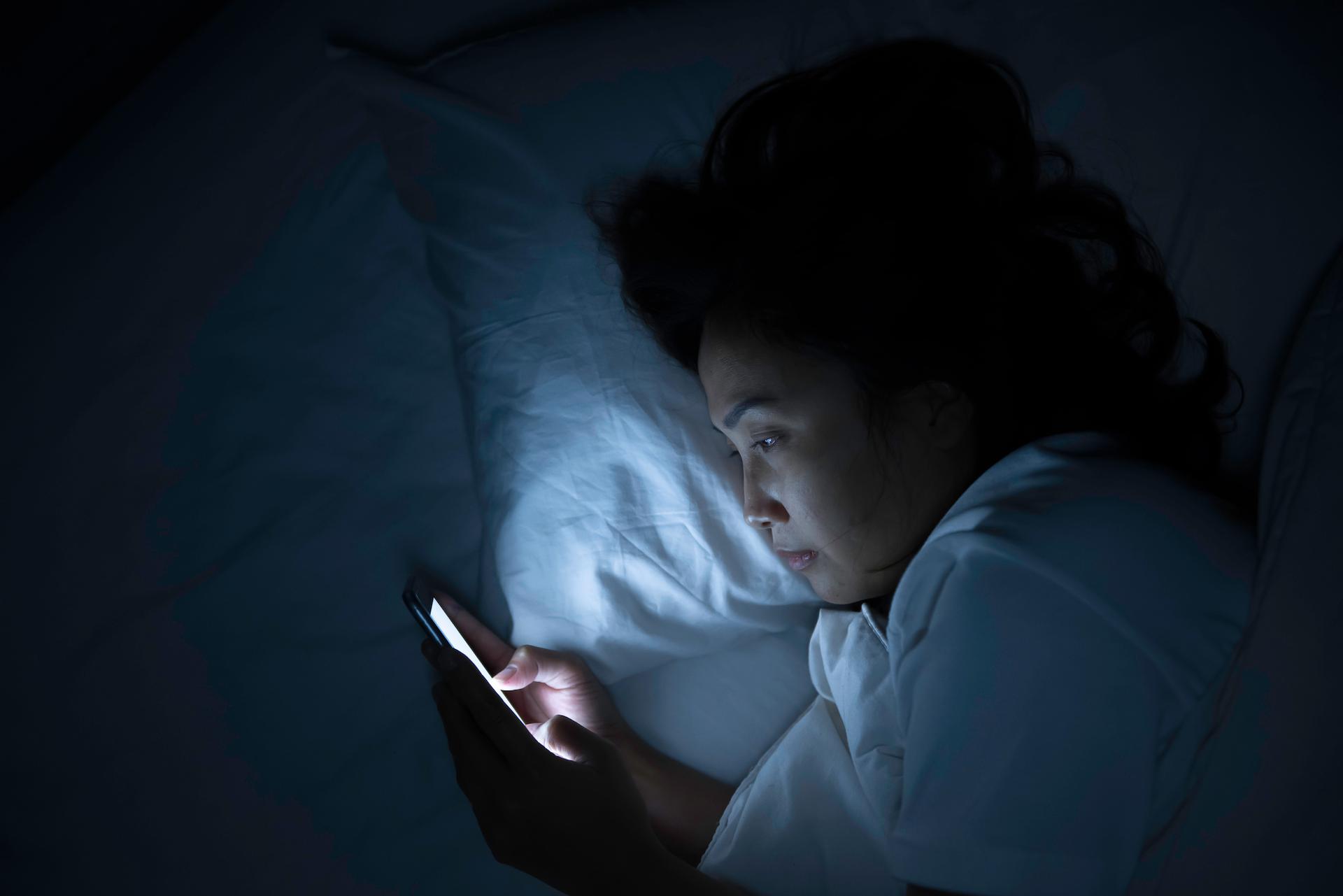 A young person looks at a smartphone in the dark