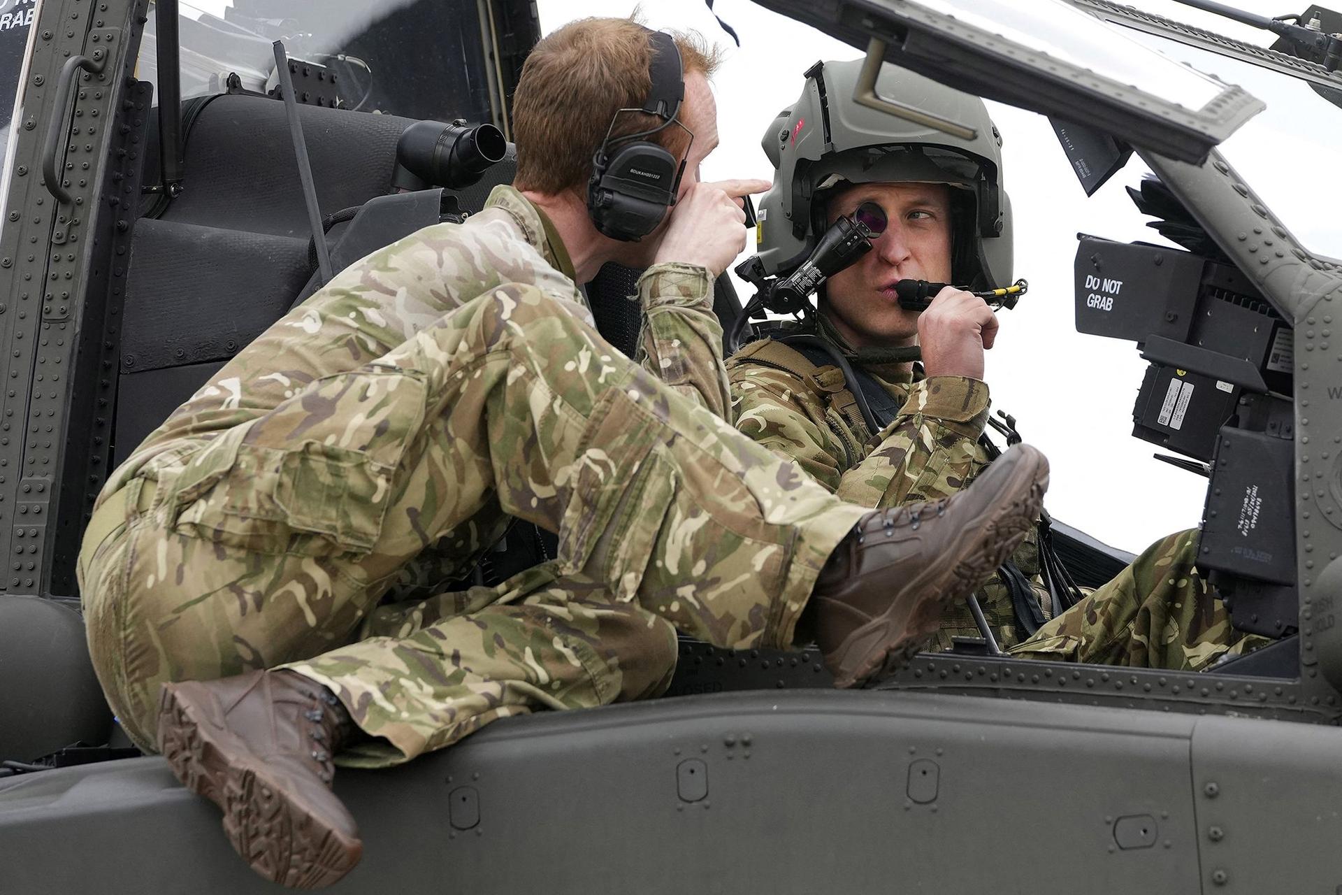 Prince of Wales (R) receives advice as he sits in the cockpit of an Apache helicopter.