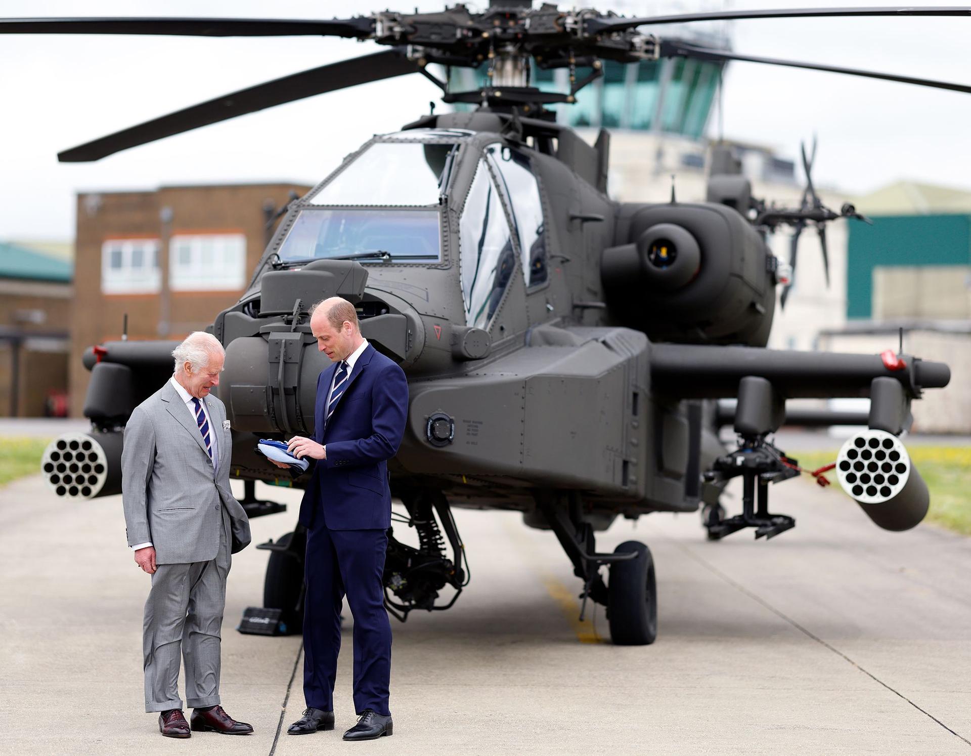 King Charles III and Prince William, Prince of Wales (both wearing the regimental tie of the Army Air Corps) stand in front of an Apache helicopter during the official handover in which The King passes the role of Colonel-in-Chief of the Army Air Corps to The Prince of Wales and presents him with the blue beret and belt of the Army Air Corps at the Army Aviation Centre, Middle Wallop on May 13, 2024 in Stockbridge, England. 