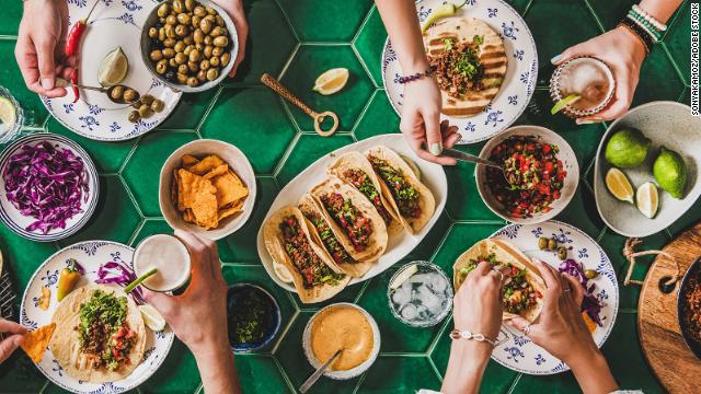 Several people serve themselves tacos and toppings