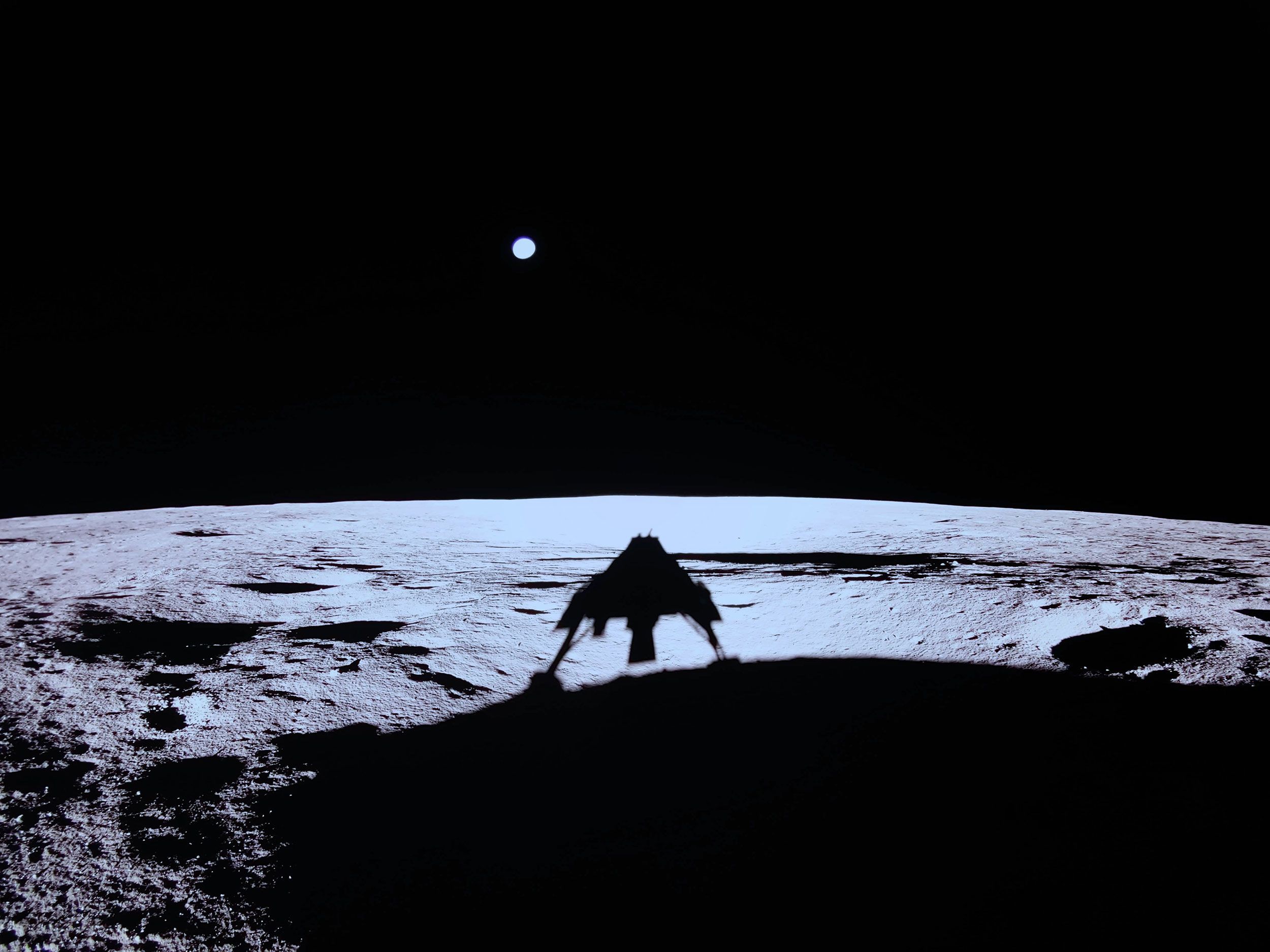 The shadow of the Blue Ghost lander can be seen on the lunar surface, with Earth visible above it. 